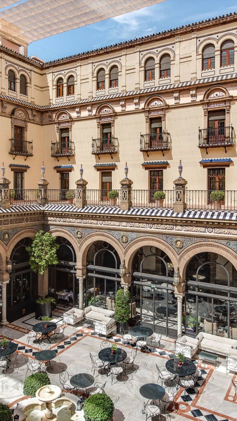 Alfonso XIII grand courtyard with Moorish arches, striped awnings and wrought-iron café tables, Seville