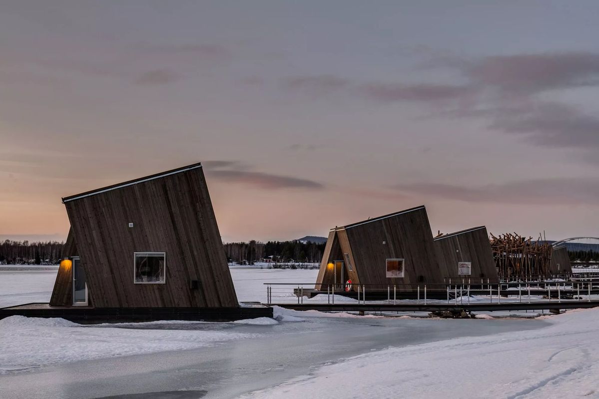 Angular timber floating cabins of Arctic Bath on the frozen Lule River at dusk, Swedish Lapland