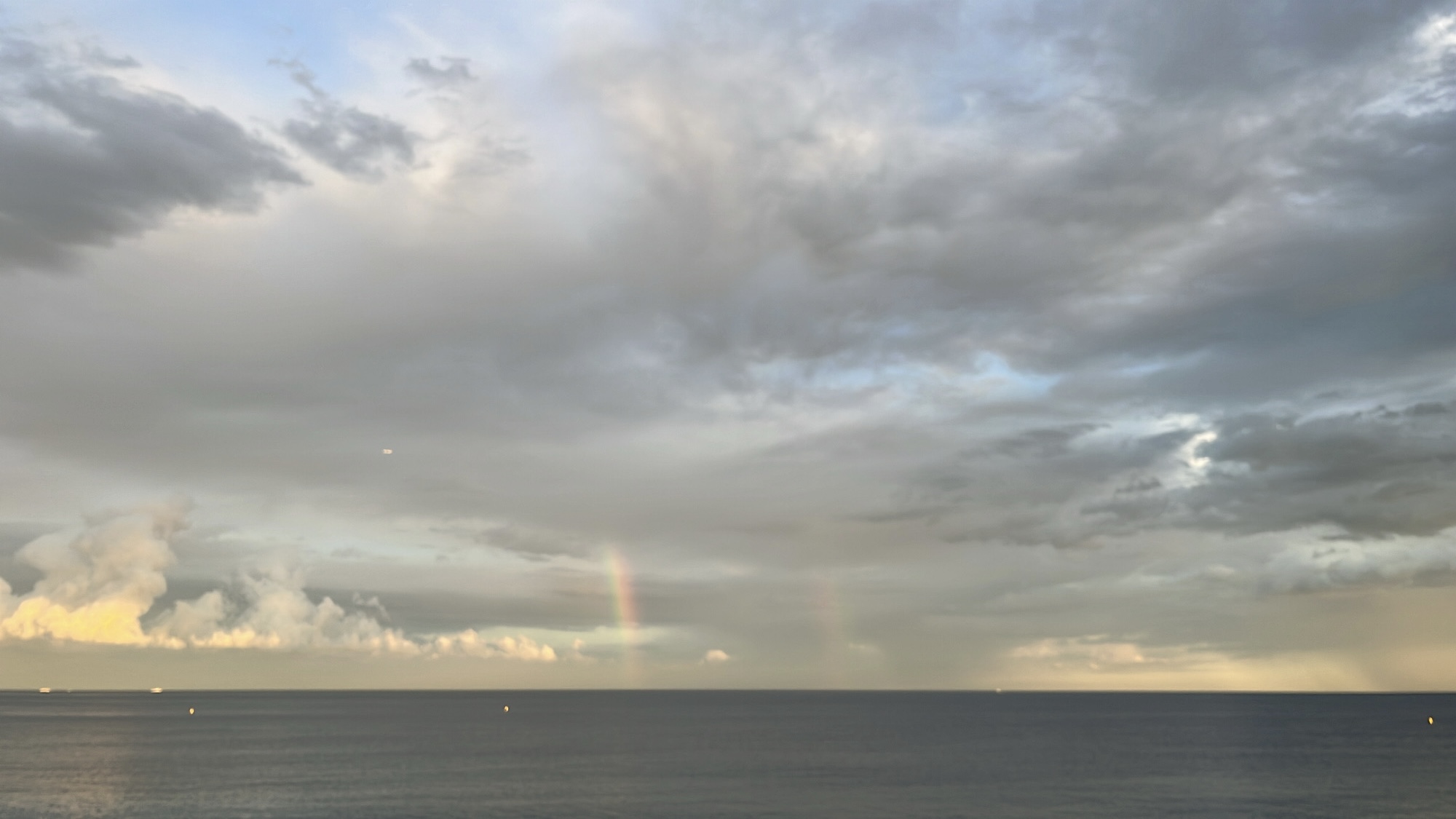 Din Tanovic — a faint double rainbow on the horizon at dusk, soft pastel clouds over the sea