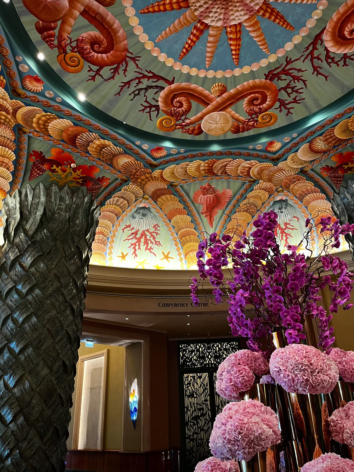 Ornate seashell and coral ceiling with magenta orchids in a grand hotel lobby