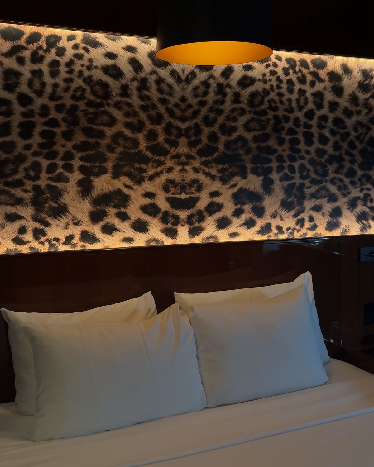Backlit leopard print headboard above a white bed