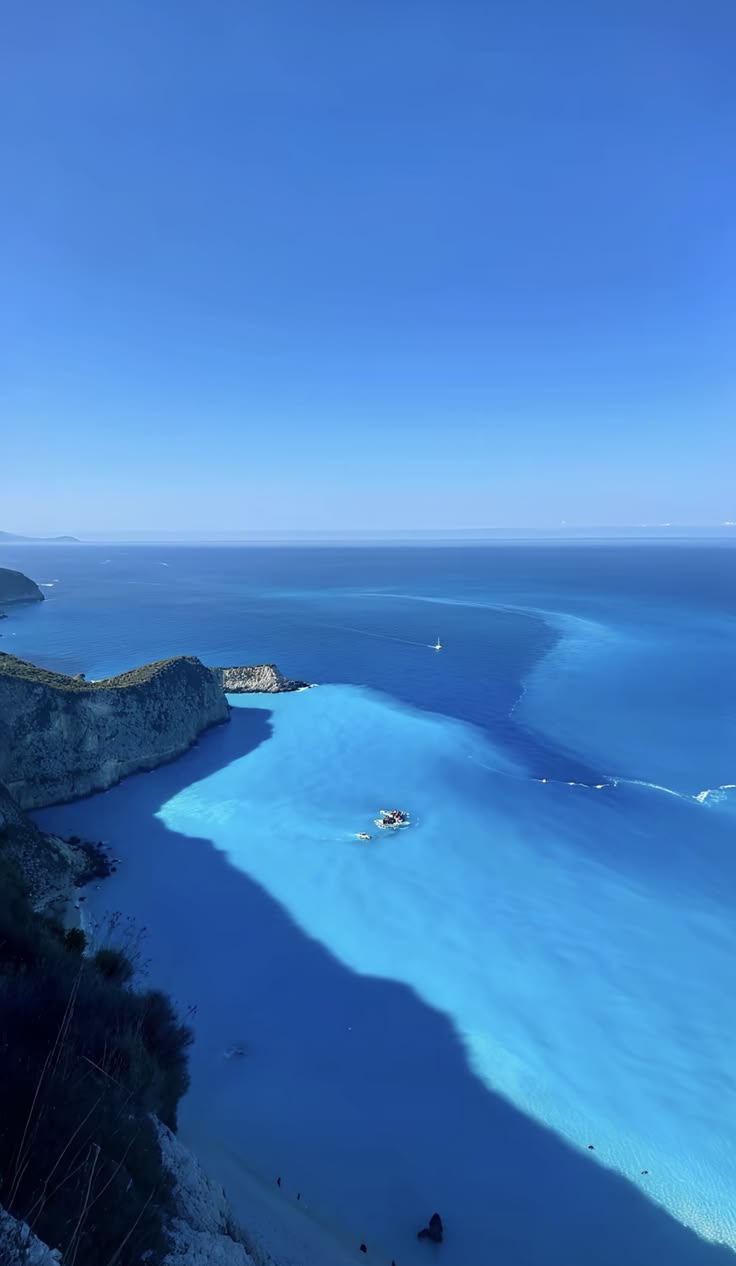 Turquoise Ionian bay seen from a cliff, tiny boat crossing the current
