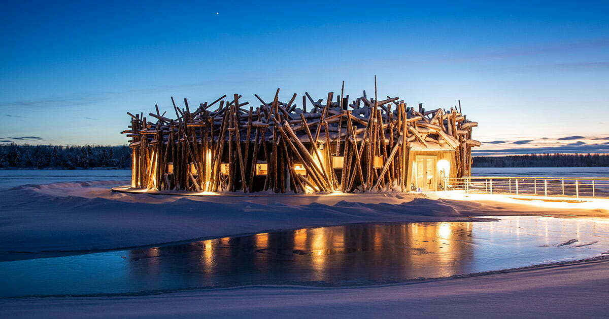Arctic Bath at twilight, its circular timber structure glowing on the frozen Lule River in Swedish Lapland