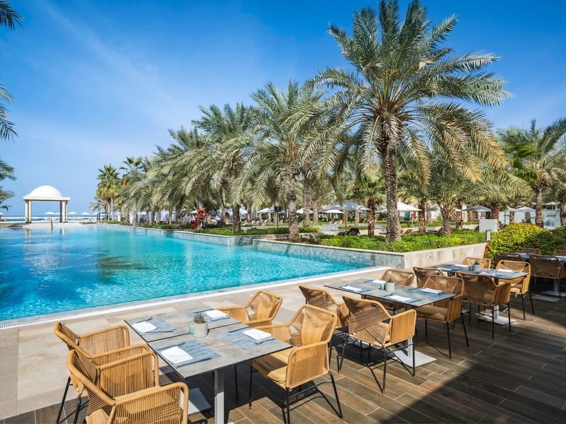 Poolside restaurant terrace overlooking the infinity pool and palm gardens during the day, Rixos Al Mairid Ras Al Khaimah