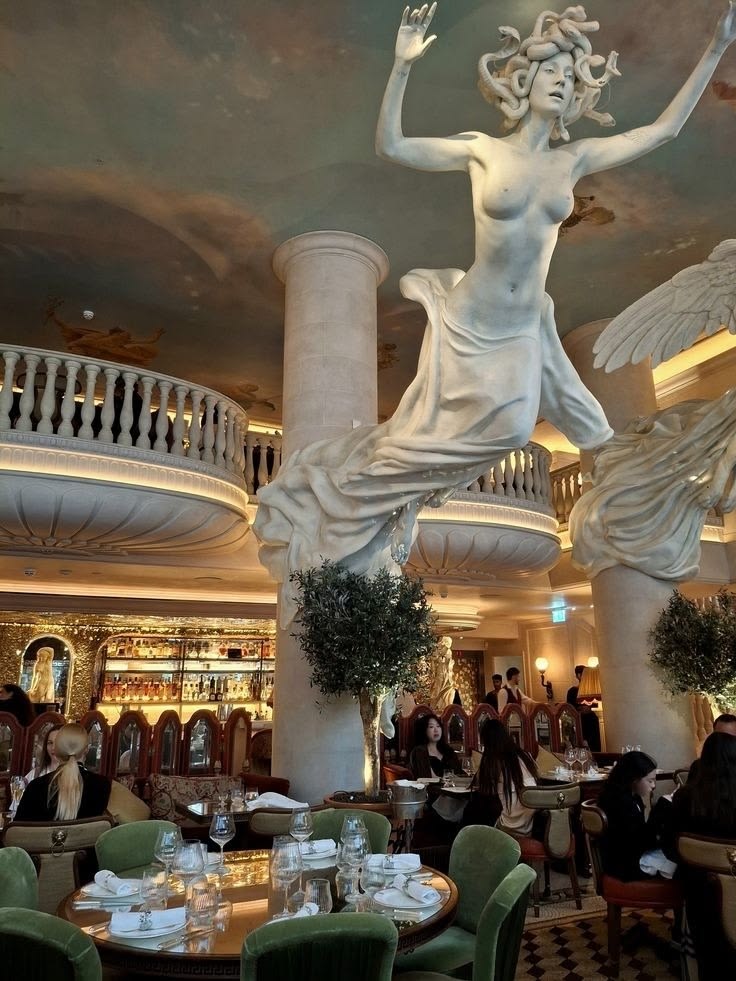 Giant Medusa statue rising through a painted-ceiling restaurant with green velvet chairs