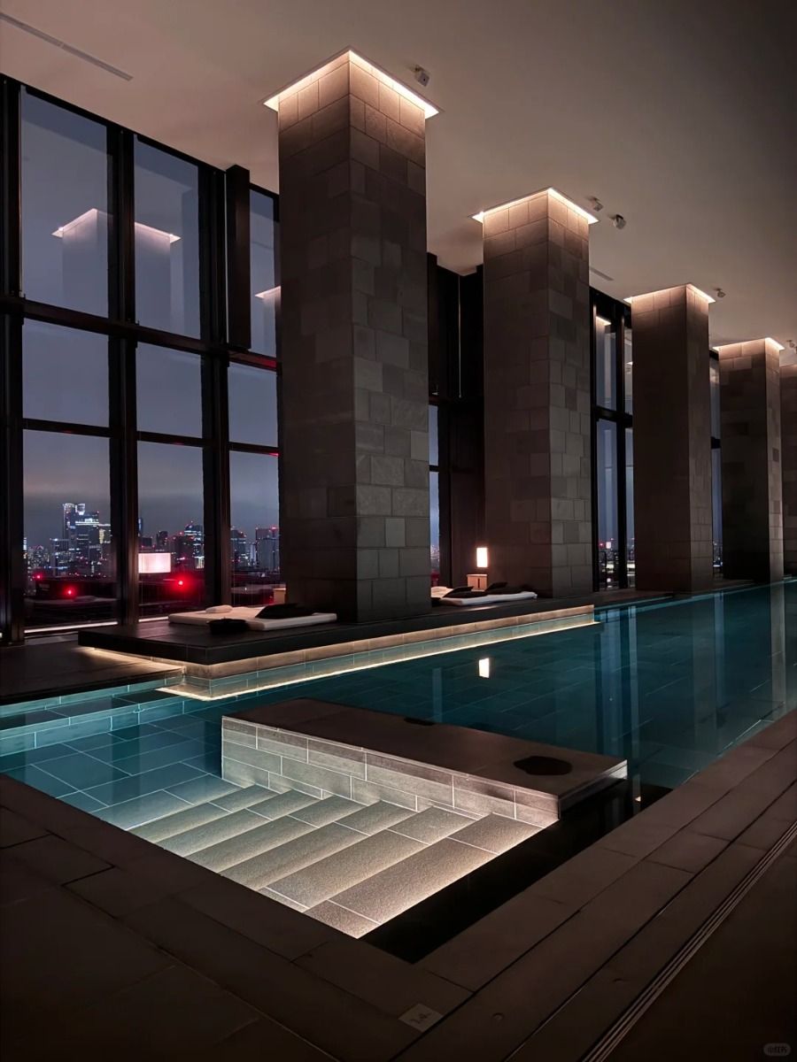 Illuminated stone columns rising beside the Aman Tokyo infinity pool with the city skyline at night