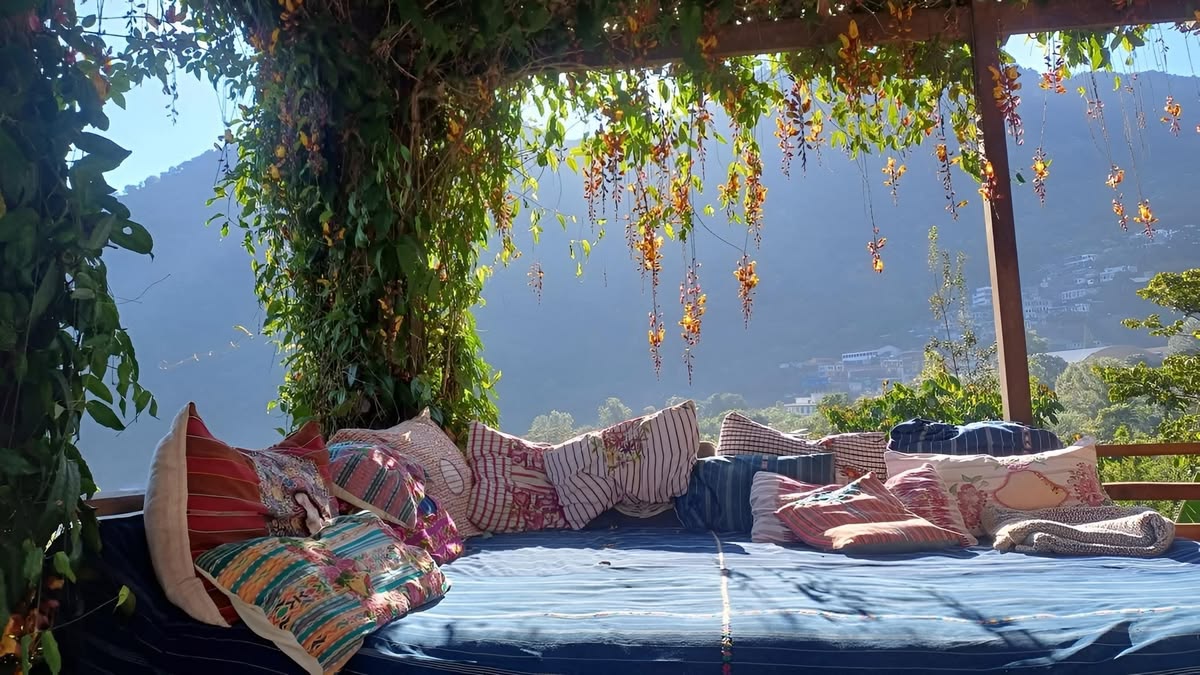 Cushioned daybed under hanging flowers with a hazy mountain view