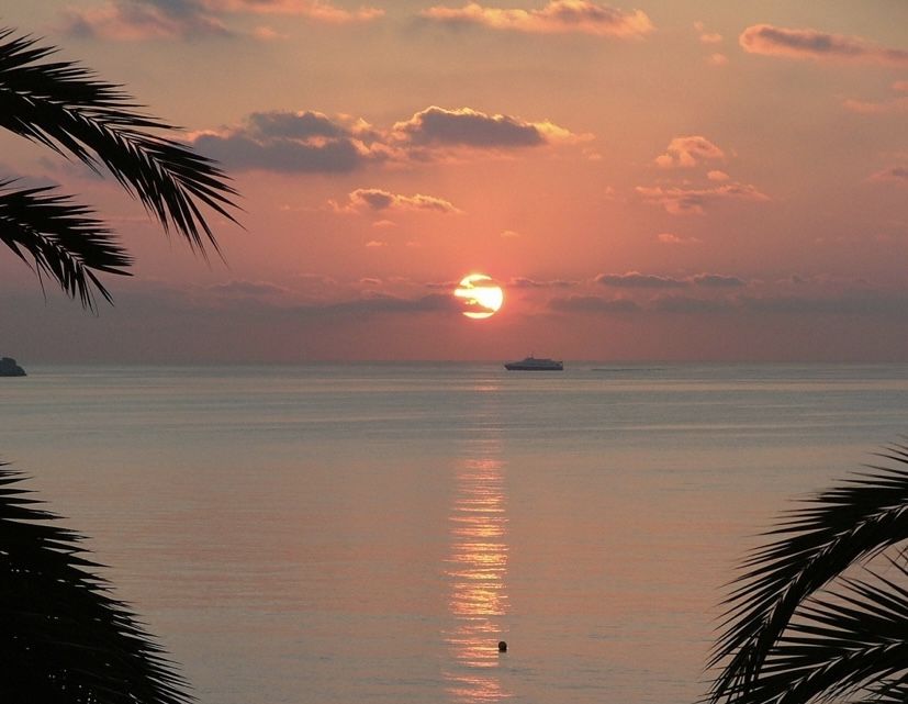 A small ferry crossing a coral-colored sunset