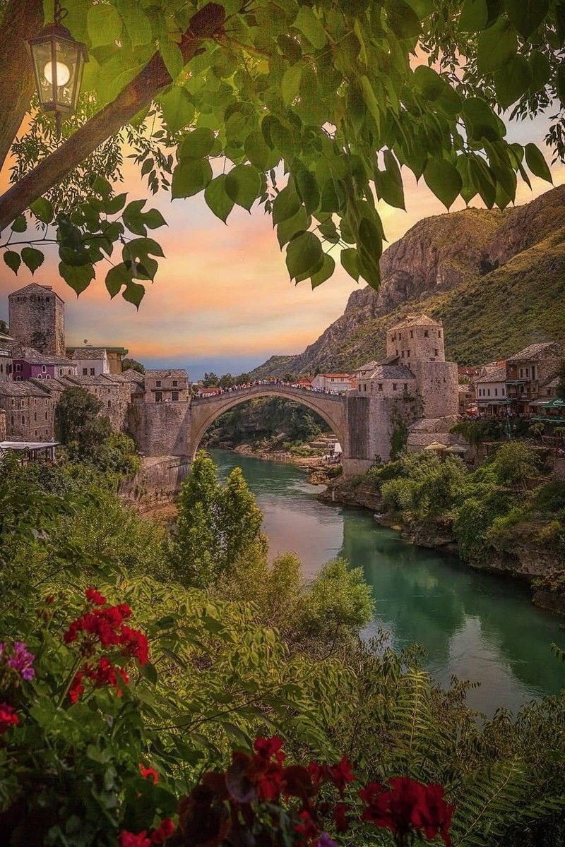 Stari Most bridge over the Neretva at sunset, framed by leaves and red flowers