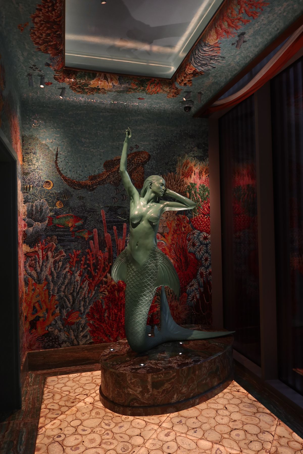 Bronze mermaid statue surrounded by a coral and mosaic hall