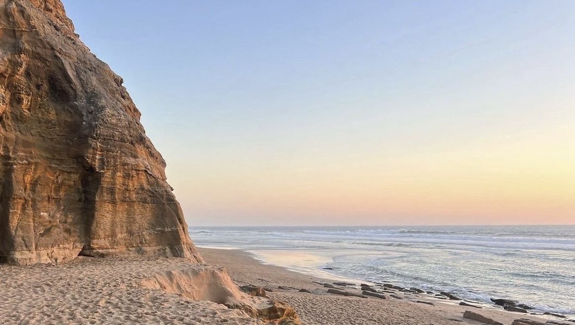 Sandstone cliff beside a pastel sunset over an empty beach
