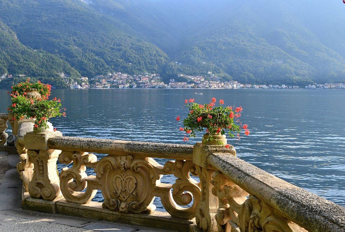 Carved stone balustrade with red geraniums overlooking Lake Como and the mountains