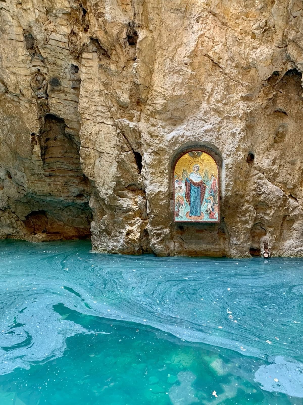 Golden mosaic icon of the Virgin Mary set into a sea cave above turquoise water