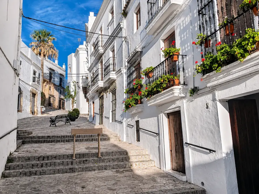 A quiet whitewashed street in Vejer de la Frontera with stone steps, wrought-iron balconies and red geraniums
